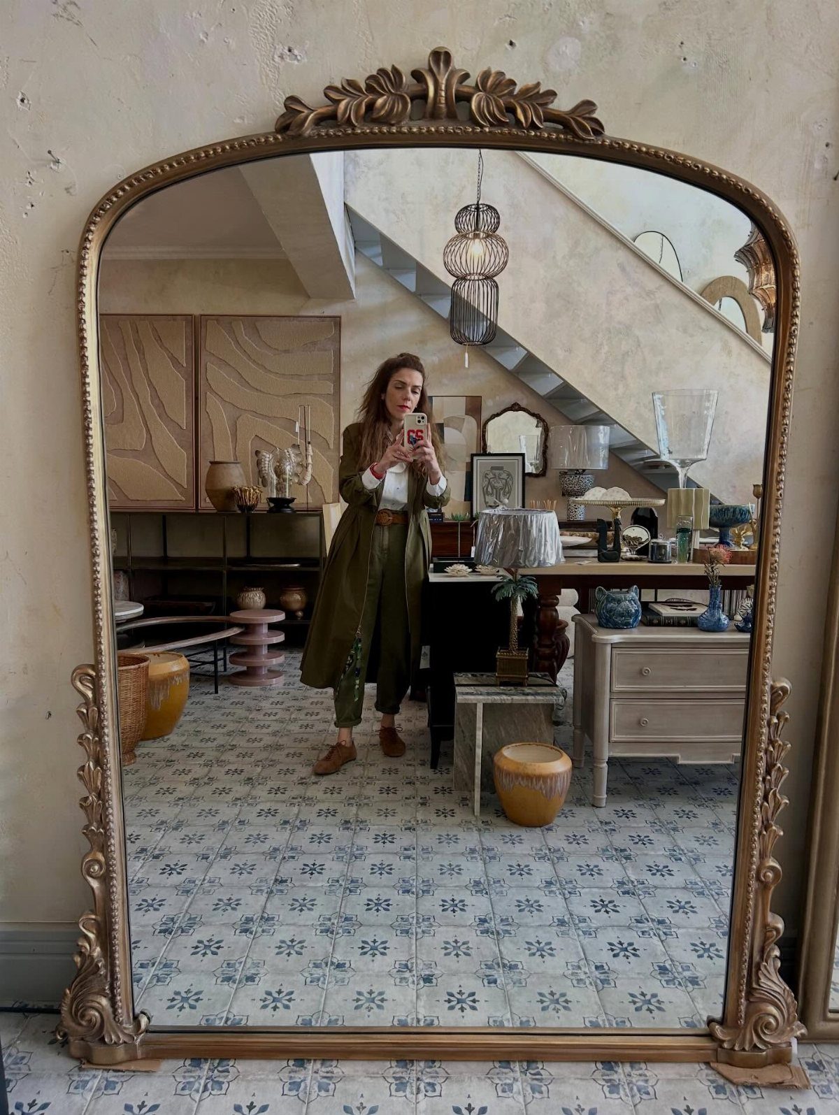 An ornate gold mirror reflecting a woman and a decorated room with patterned tiles.