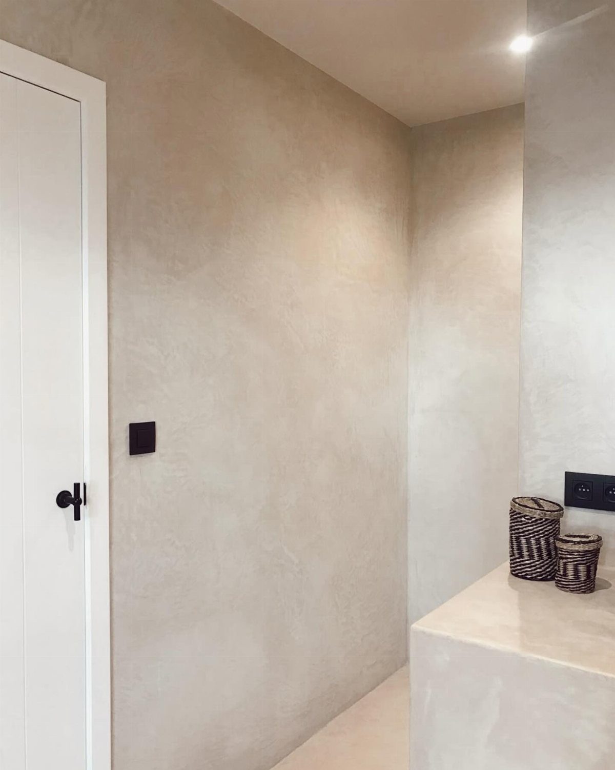 Textured beige plaster walls in a modern room with a white door and woven baskets.