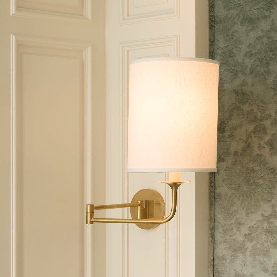 A gold wall sconce with a white drum shade mounted on a white paneled wall.