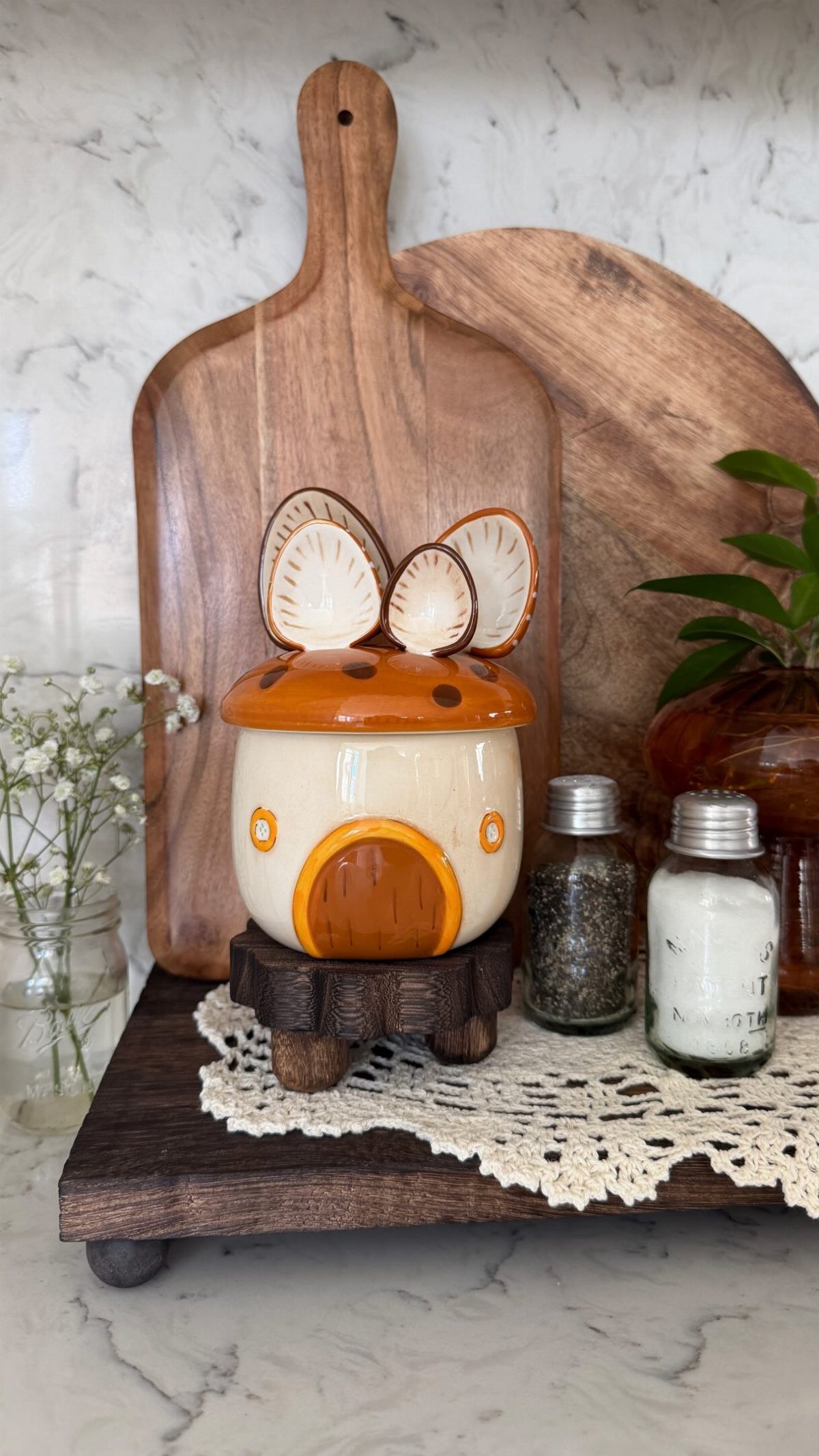 A ceramic mushroom jar on a wooden stand next to salt and pepper shakers.