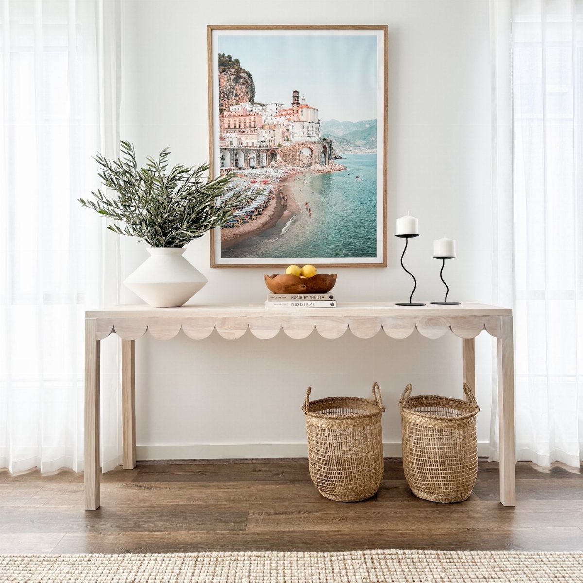 A light wood console table with scalloped edges decorated with greenery and candles.