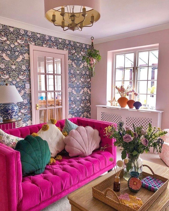 Bright pink velvet sofa with colorful shell pillows in a patterned living room.