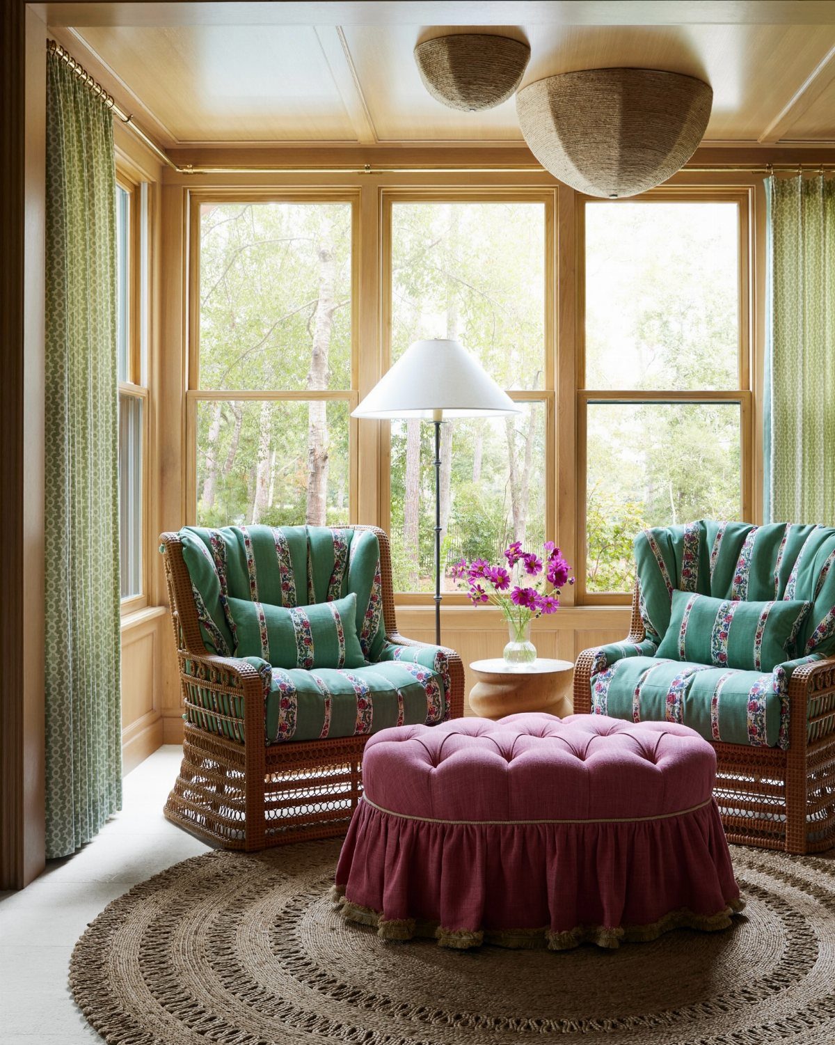 Two green patterned armchairs and a large magenta tufted ottoman in a sunlit sunroom.