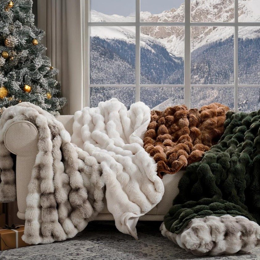 Textured faux fur throws in various colors draped over a cream sofa near a snowy window.