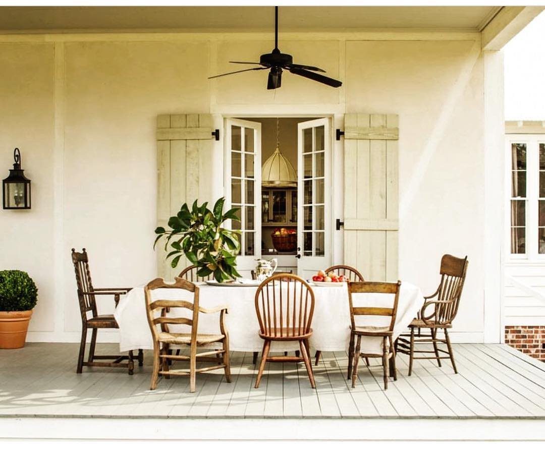 Mismatched wooden dining chairs arranged around a white table on a covered porch.
