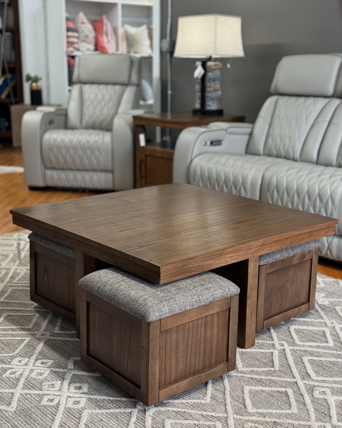 Wooden coffee table with four grey upholstered ottomans tucked underneath on a patterned rug.