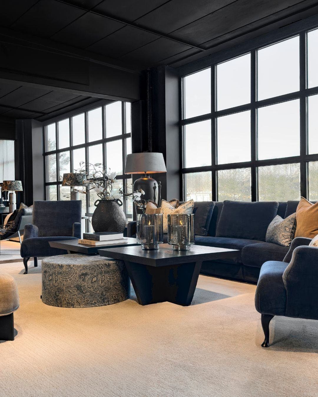Navy blue velvet seating and a textured ottoman arranged around a black coffee table.