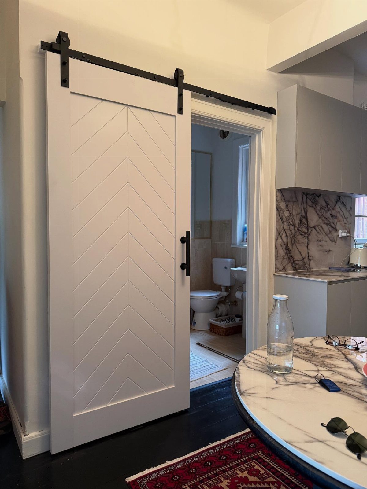 White chevron patterned sliding barn door on a black metal track opening into a bathroom.