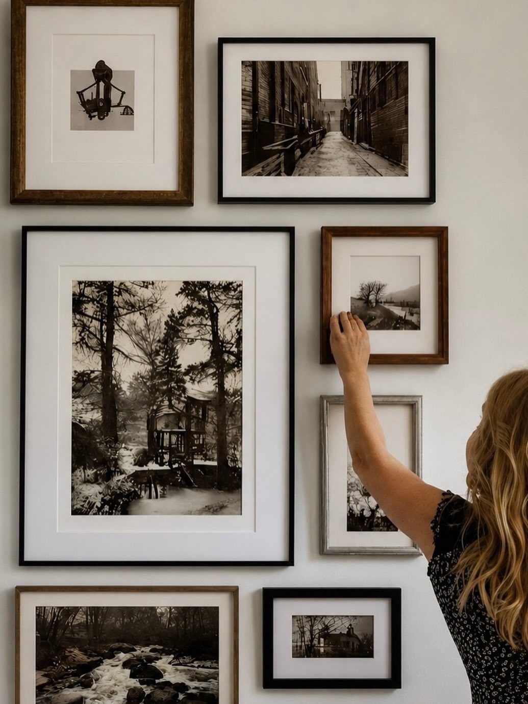 A person hanging a small framed black and white photograph onto a gallery wall.