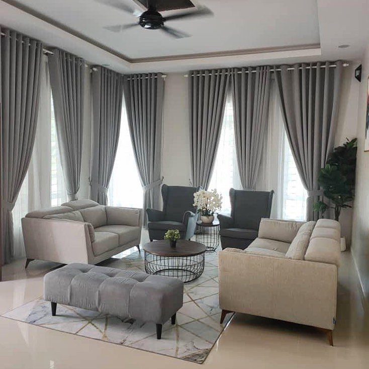 Grey sofas, armchairs, and an ottoman arranged in a modern living room with matching curtains.