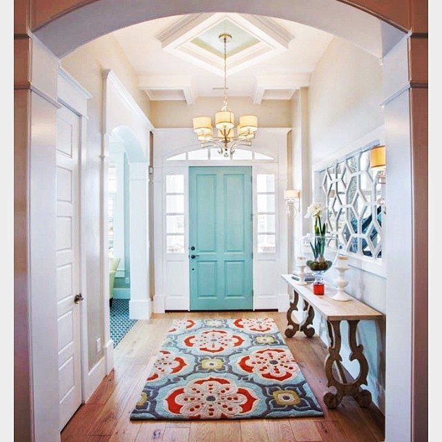 A bright hallway with a teal door and a vibrant patterned rug.