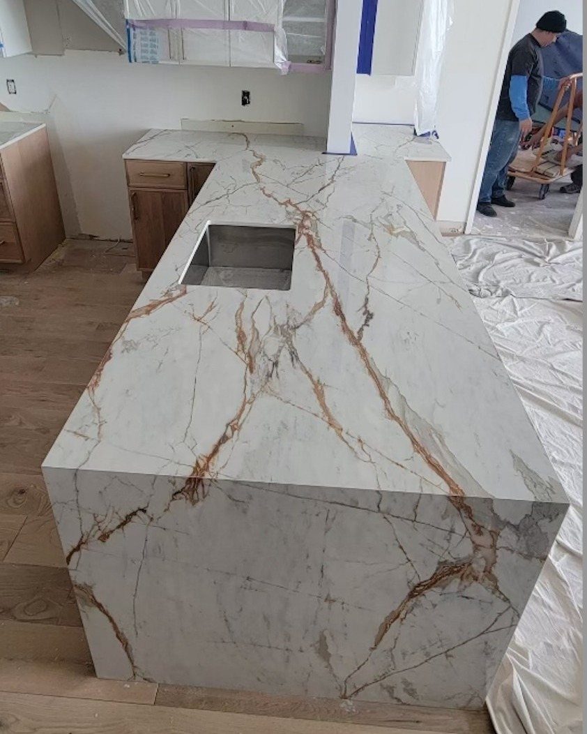 A white marble kitchen island with gold veining and a waterfall edge design.