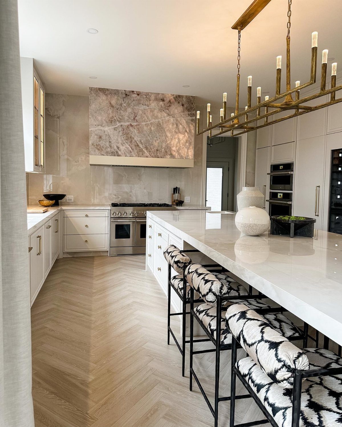 Modern kitchen with white marble island, patterned bar stools, and herringbone wood flooring.