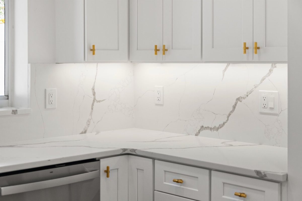 White marble countertops with matching marble backsplash and gold hardware on white cabinets.