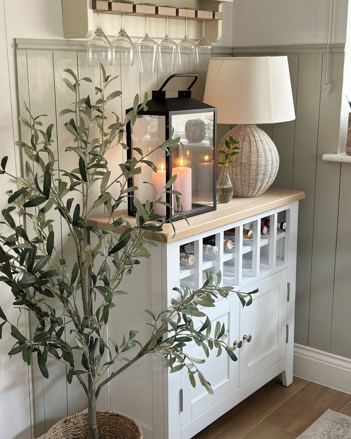 A white sideboard with a built-in wine rack, a lantern, and a wicker lamp.