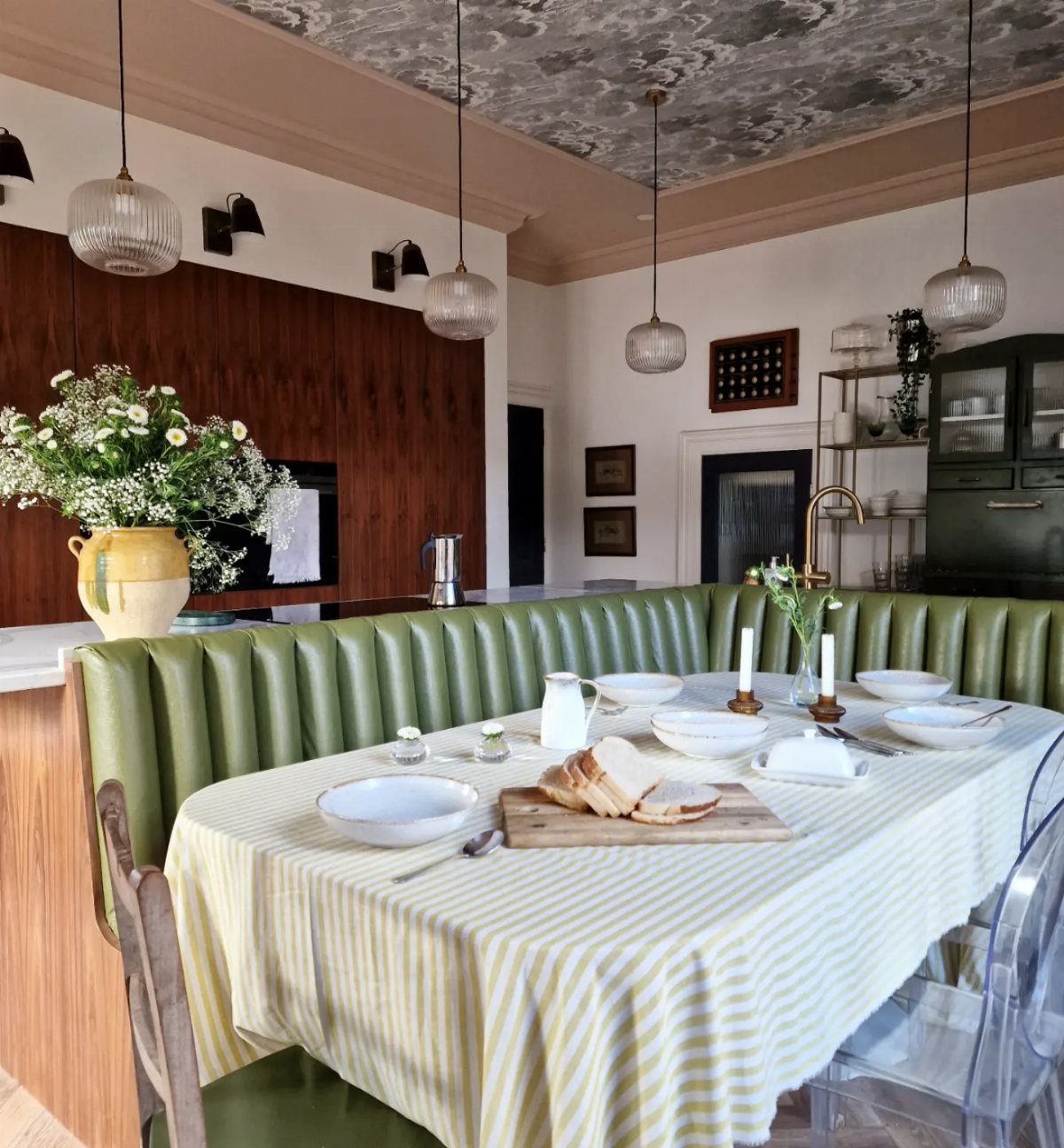 A dining table with yellow striped cloth and green banquette seating in a stylish room.