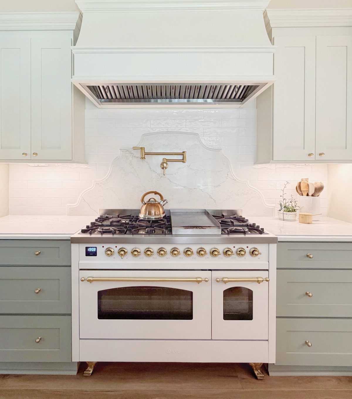 White professional gas range with brass accents and a marble backsplash in a sage green kitchen.