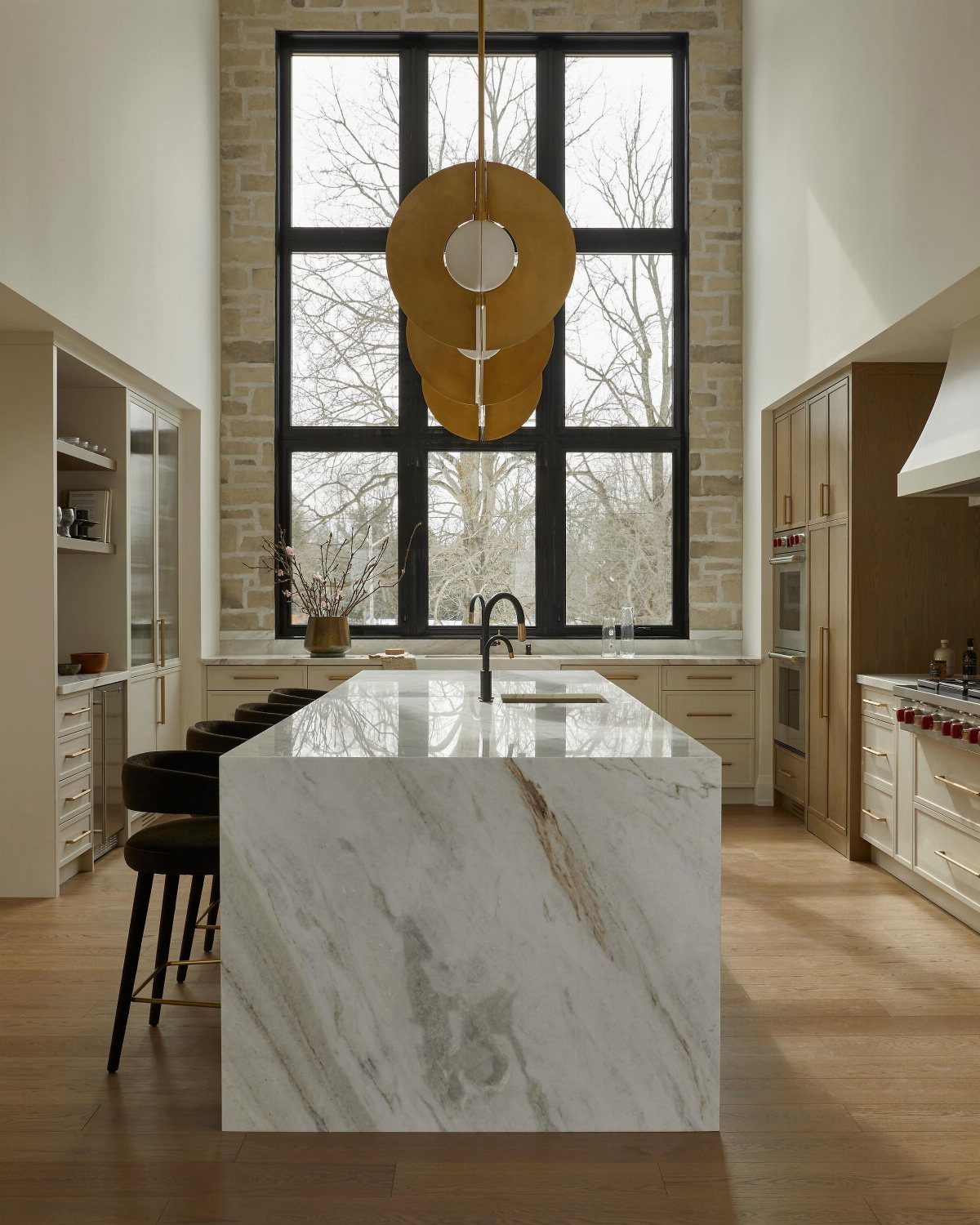 Large marble waterfall island in a modern kitchen with high ceilings and a massive window.