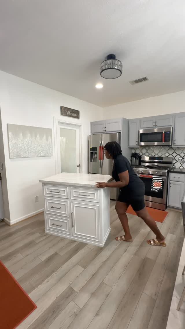 A woman pushing a white portable kitchen island across a light wood floor.