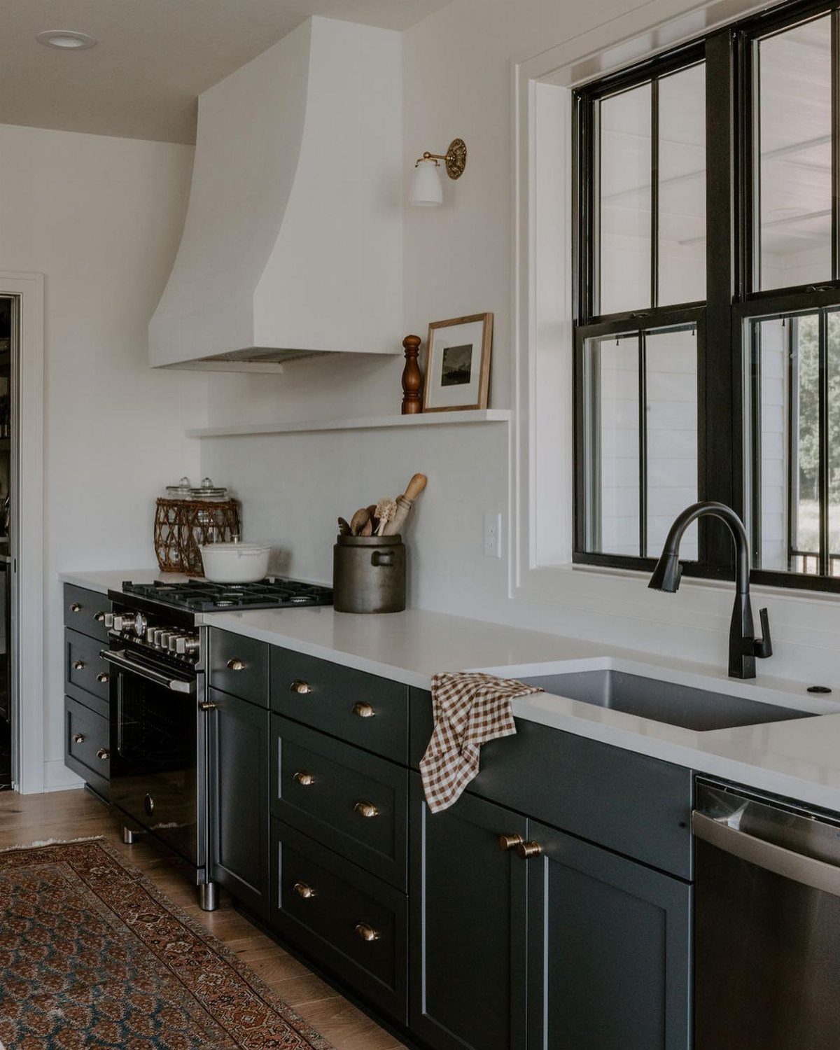 Dark navy kitchen cabinets with brass handles, white countertops, and a black window frame.