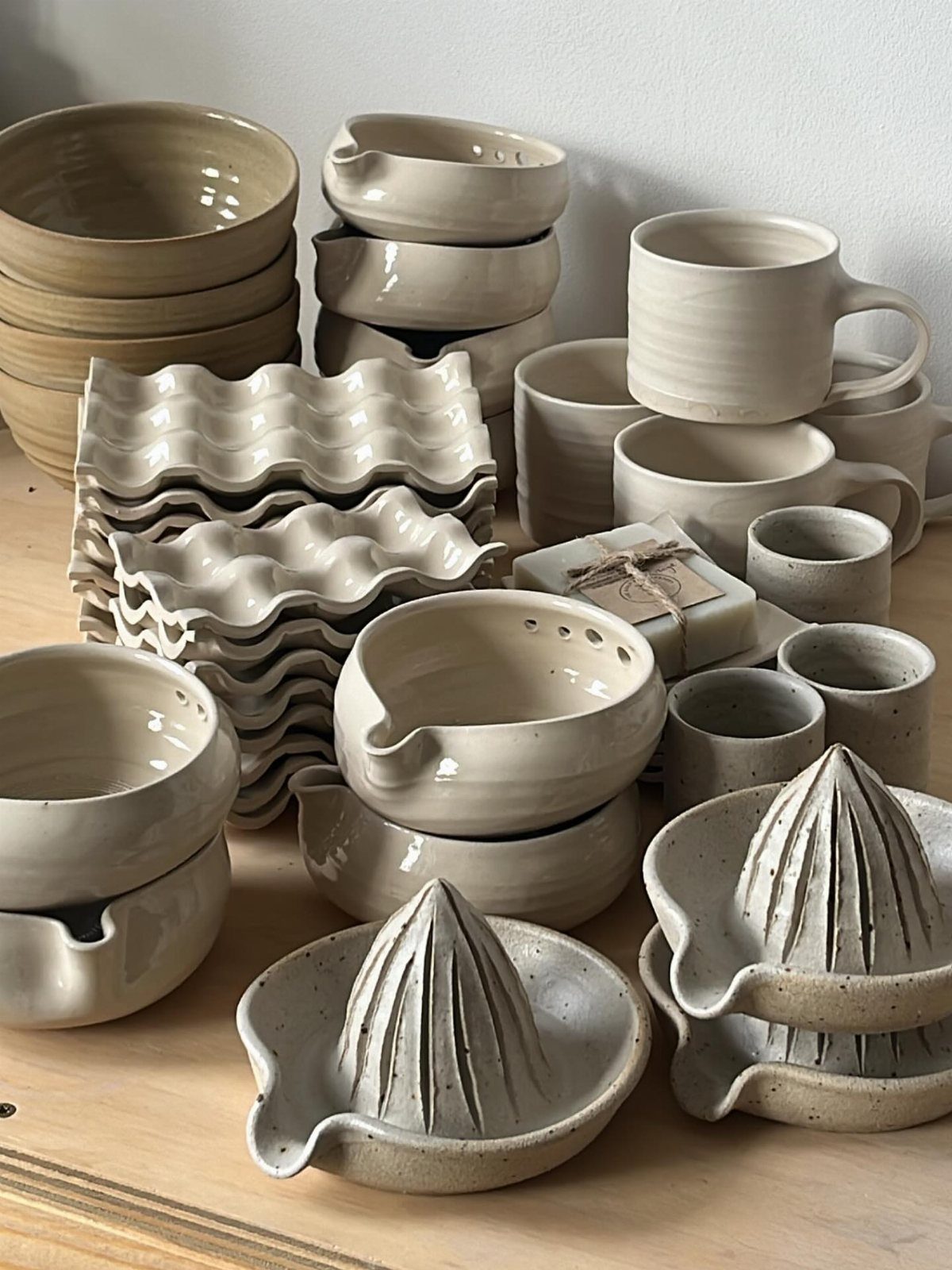 Assorted cream-colored ceramic bowls, mugs, and wavy plates arranged on a wooden surface.