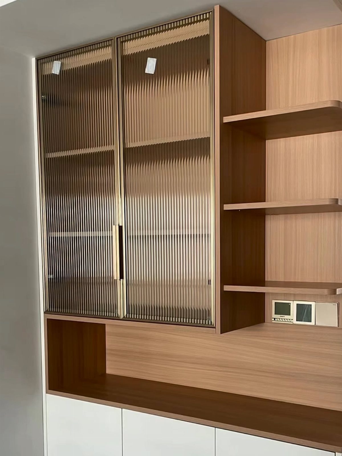 Fluted glass cabinet doors with gold frames integrated into a light wood kitchen storage unit.
