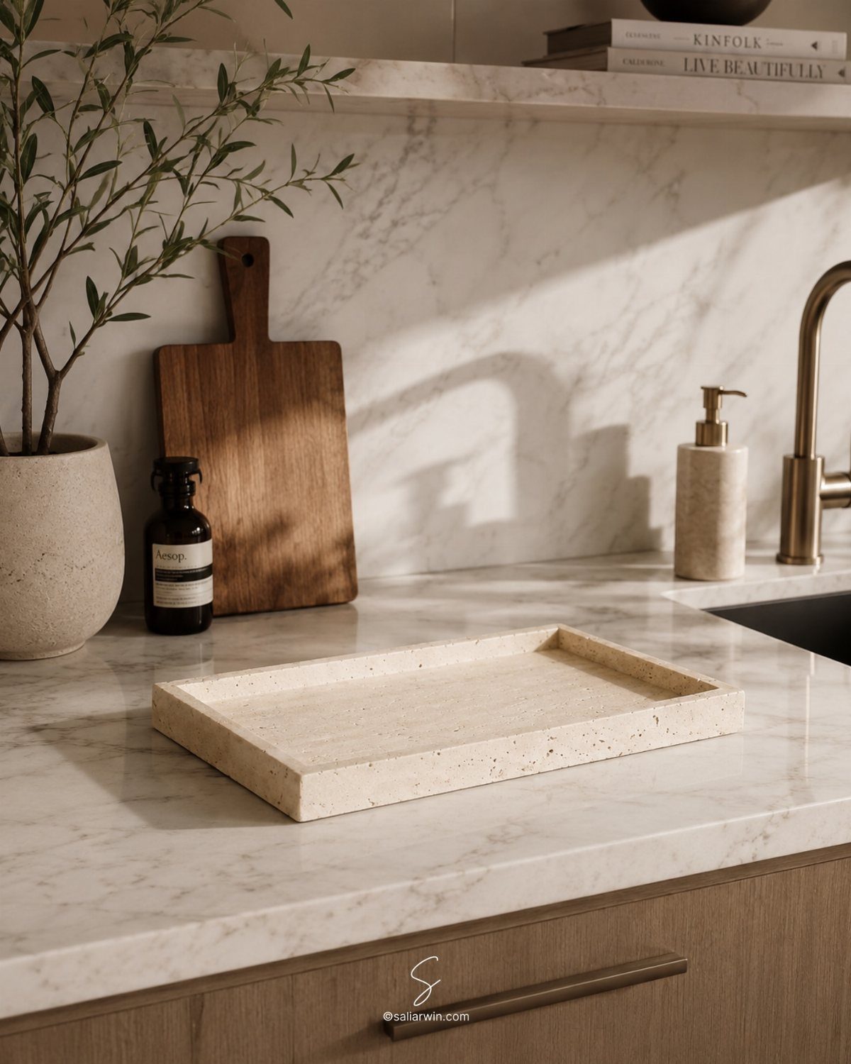 A speckled beige tray sits on a marble countertop next to a wooden cutting board and olive plant.