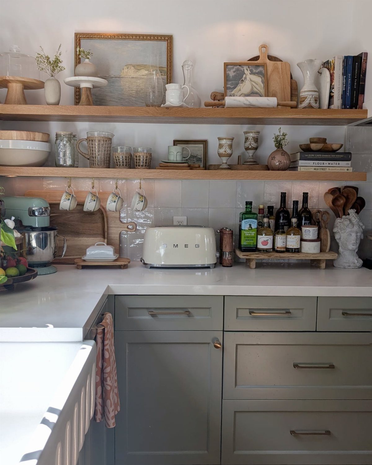 Wooden open shelves filled with ceramic dishes, glassware, and framed art above a white kitchen counter.