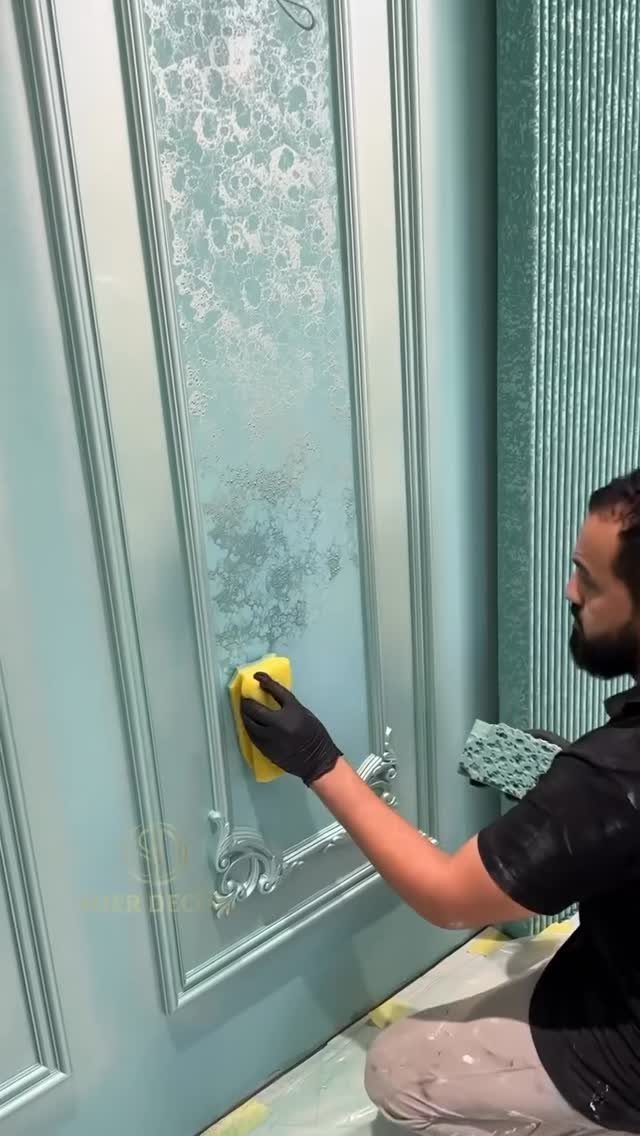 A person applies a textured silver finish to a seafoam green decorative cabinet door.