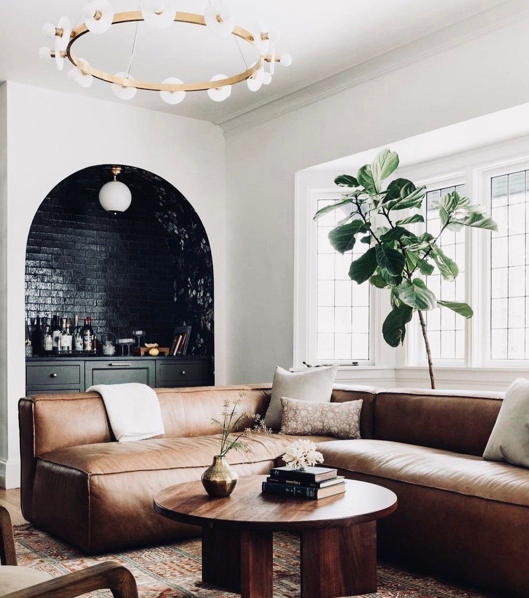 A built-in black arched bar area situated behind a brown leather sectional sofa.