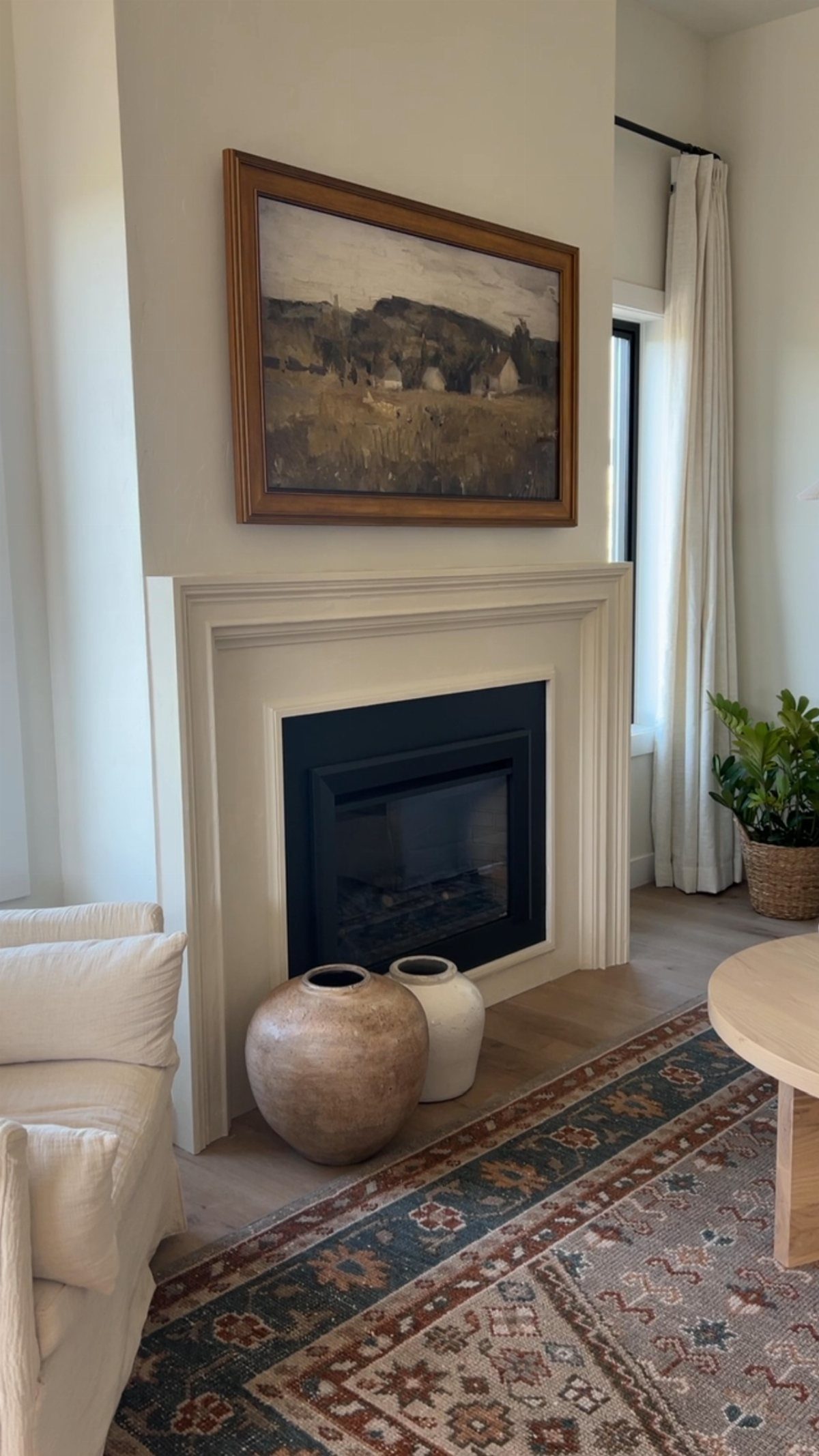 A large framed landscape painting hanging above a white fireplace in a modern living room.