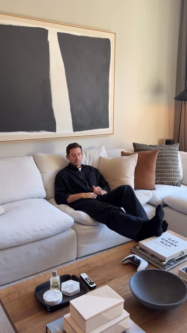 A man relaxes on a white sofa beneath a large black and white abstract painting.