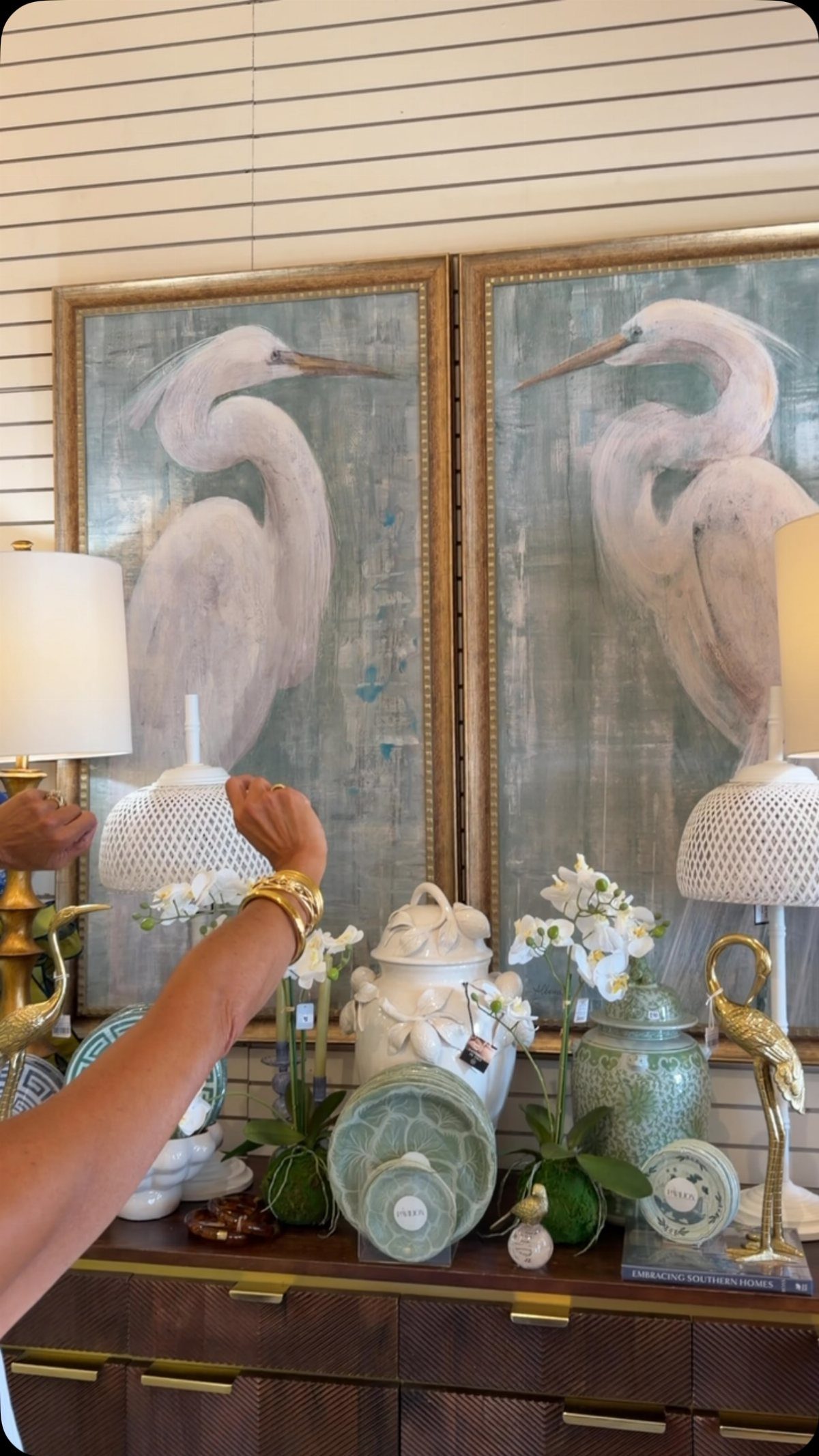 Two large heron paintings in gold frames sit above decorative ceramic jars and lamps.