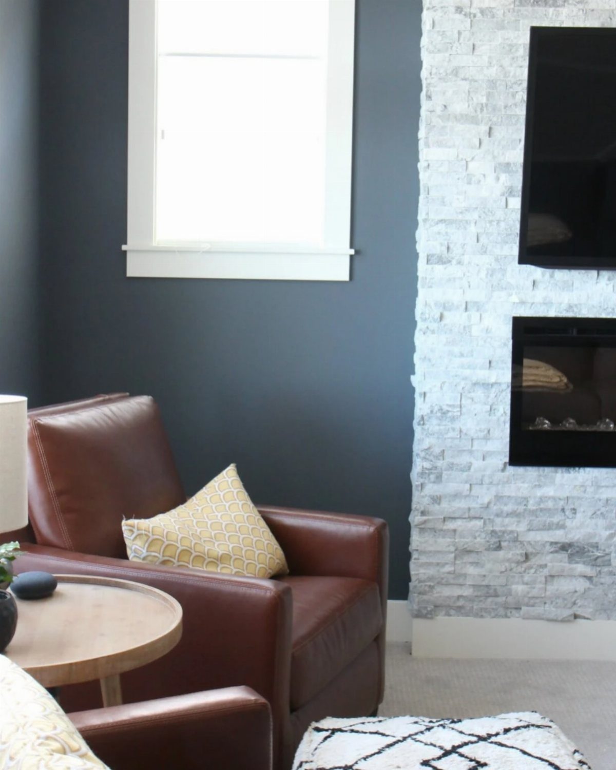 Brown leather armchair with a yellow pillow sits next to a dark blue wall and stone fireplace.