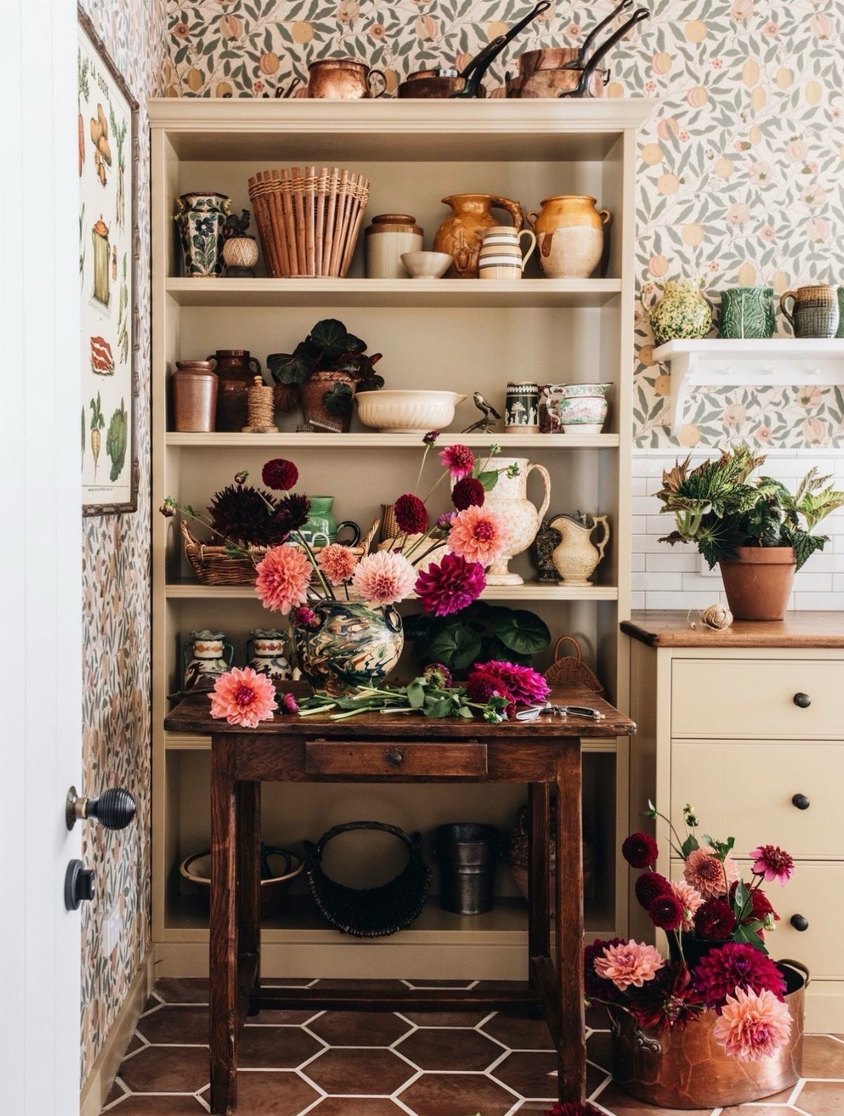 Vintage wooden hutch filled with ceramics and baskets next to a floral arrangement on a table.