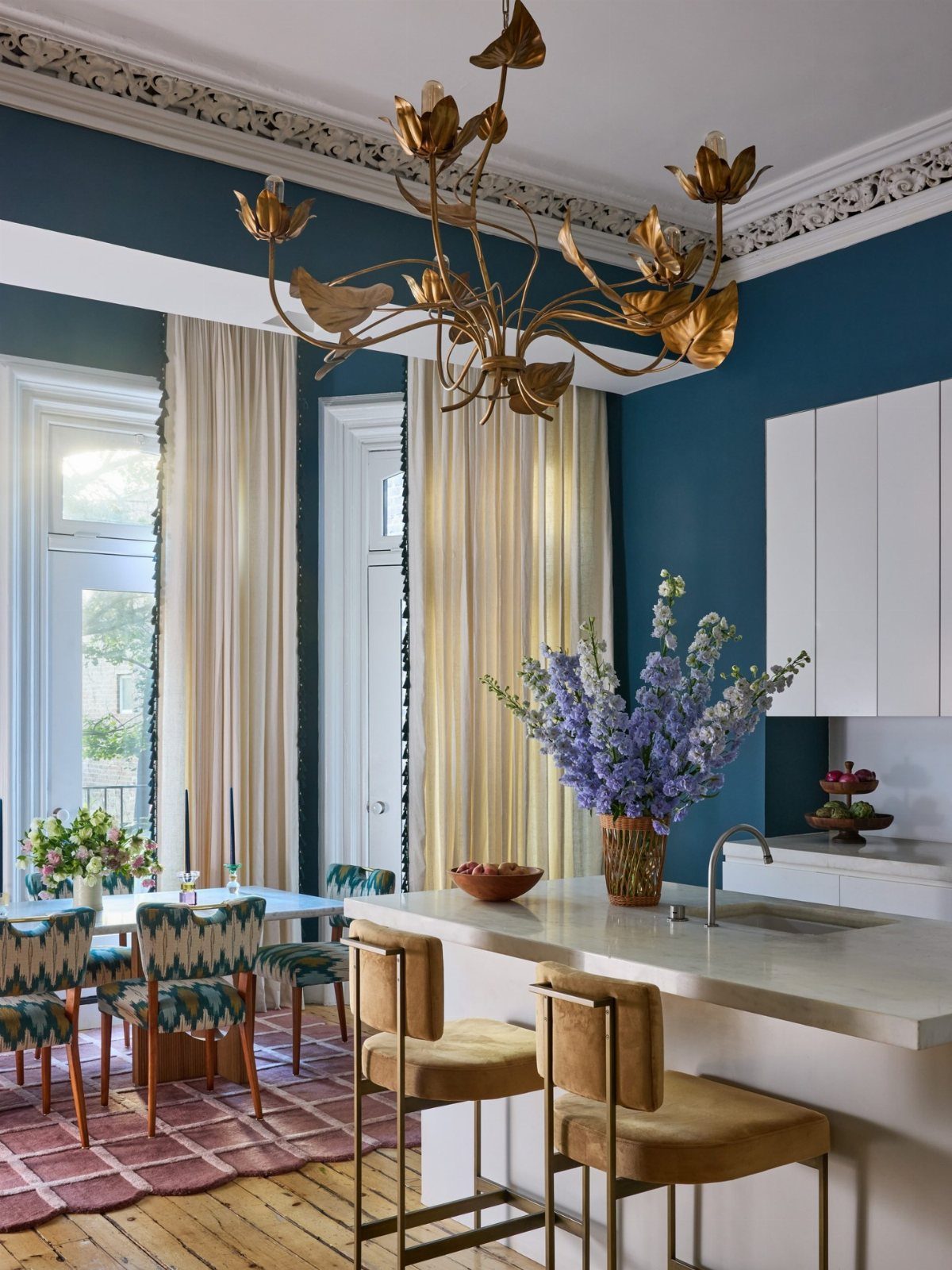 A large gold leaf-shaped chandelier hanging in a teal dining room with cream curtains.