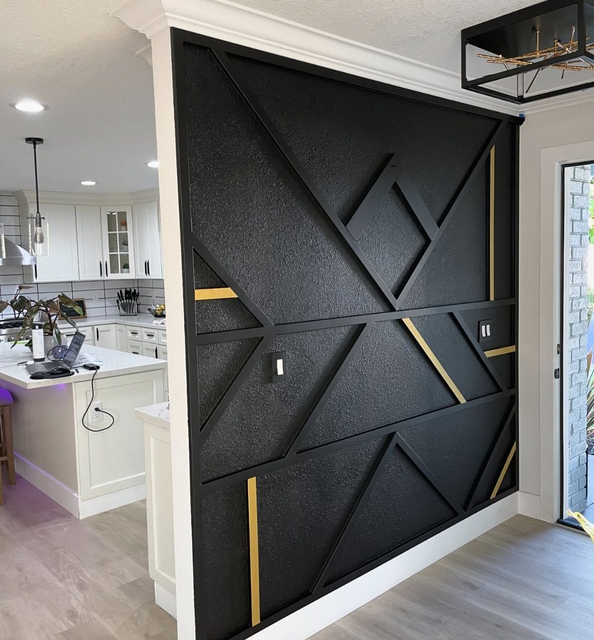 Black geometric accent wall with gold metallic inlay strips in a modern home interior.