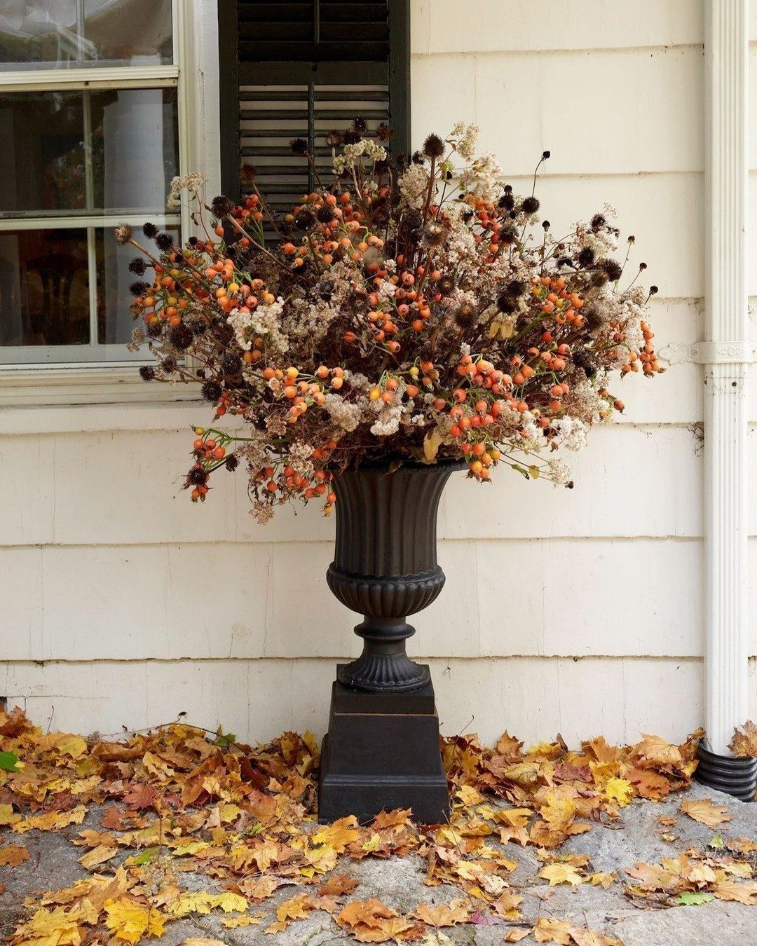 Large dark urn filled with dramatic dried orange berries and autumn floral arrangements.