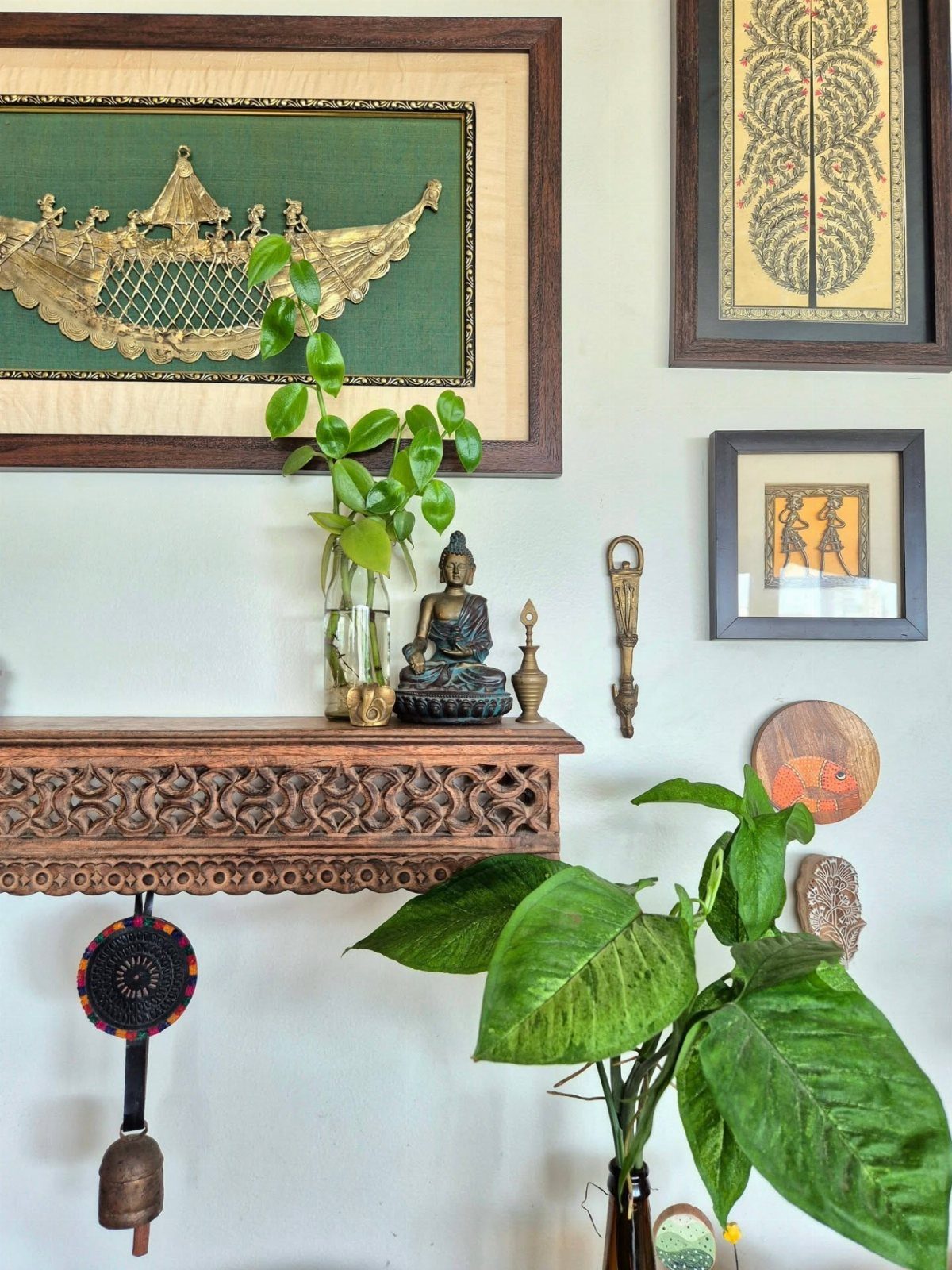 Framed eclectic art pieces and a Buddha statue sit on a carved wooden shelf.