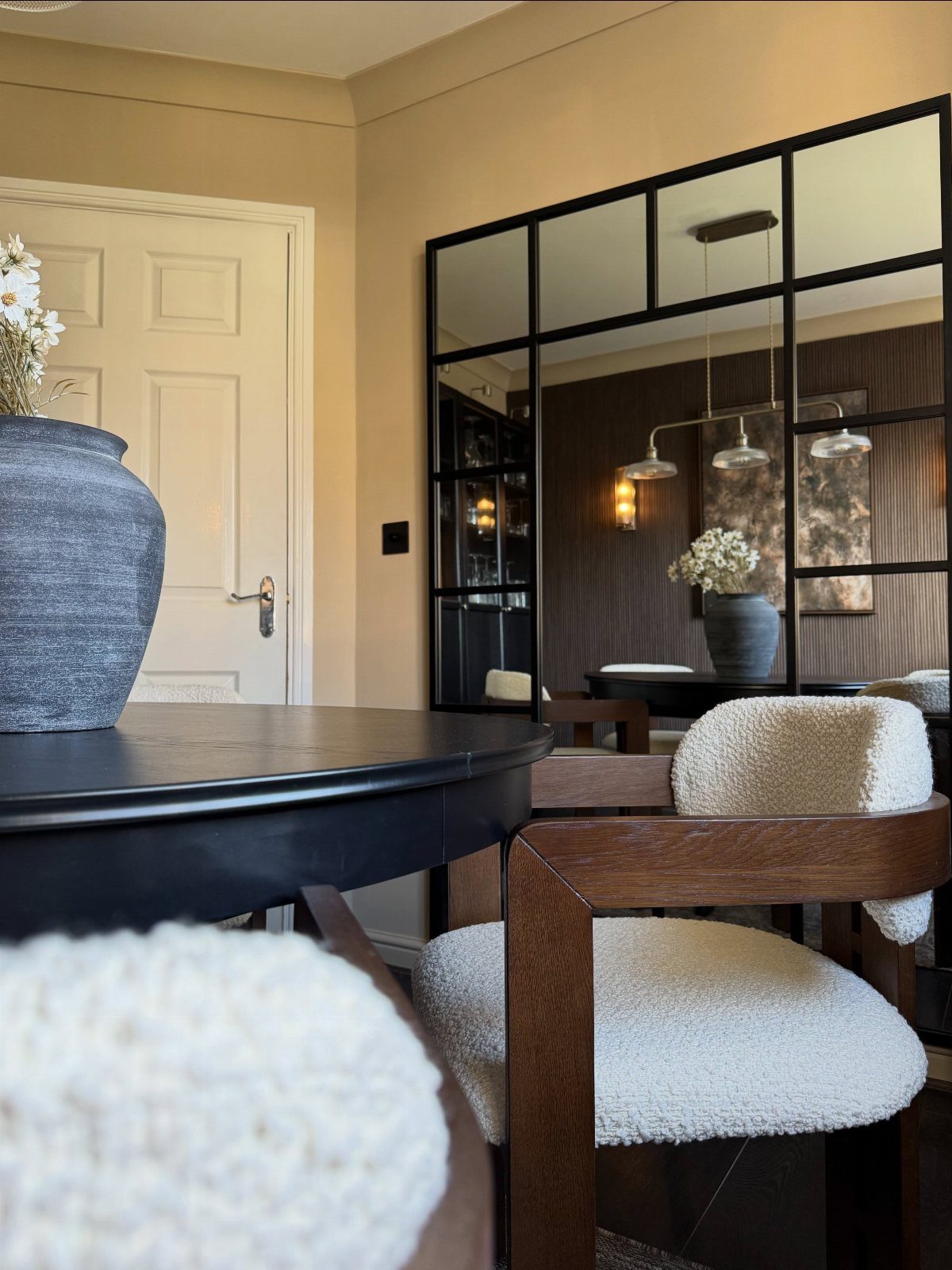 Large black-framed window-pane mirror reflecting a dark dining room with pendant lights and chairs.