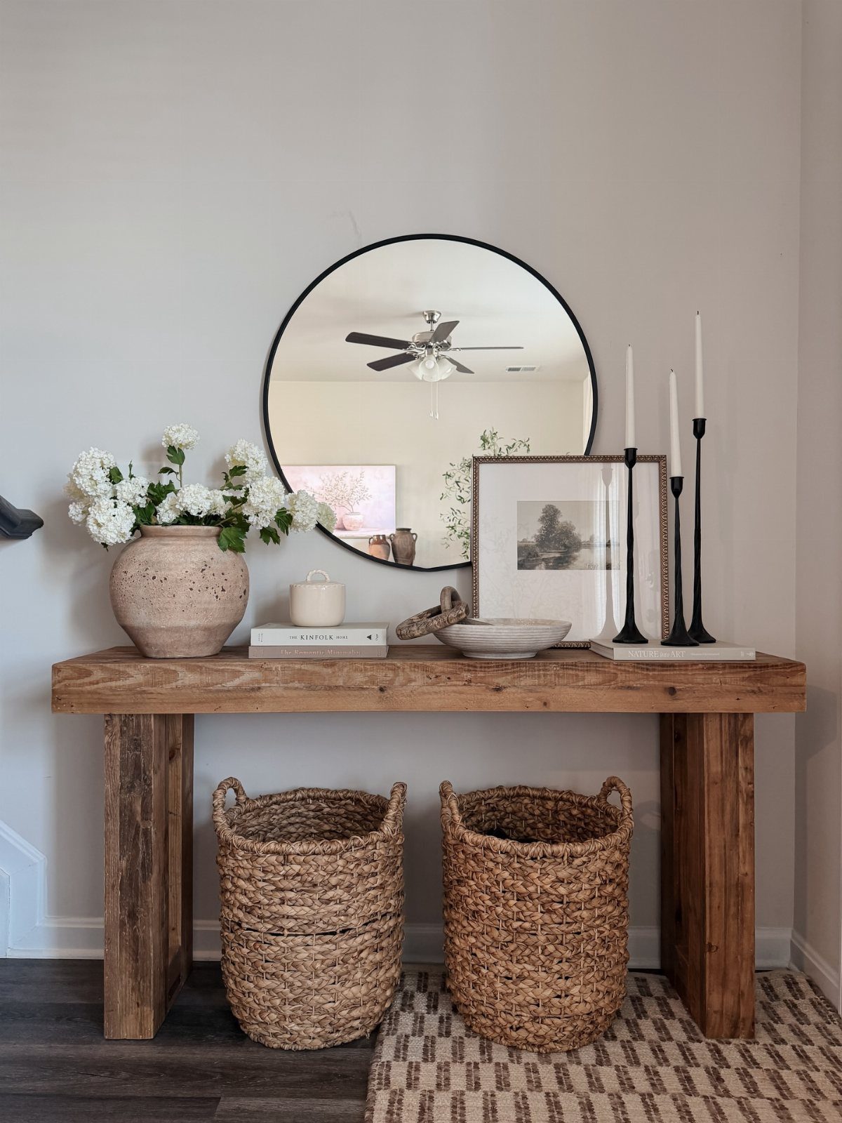 Rustic wooden console table featuring a round mirror, white flowers, and black taper candles.