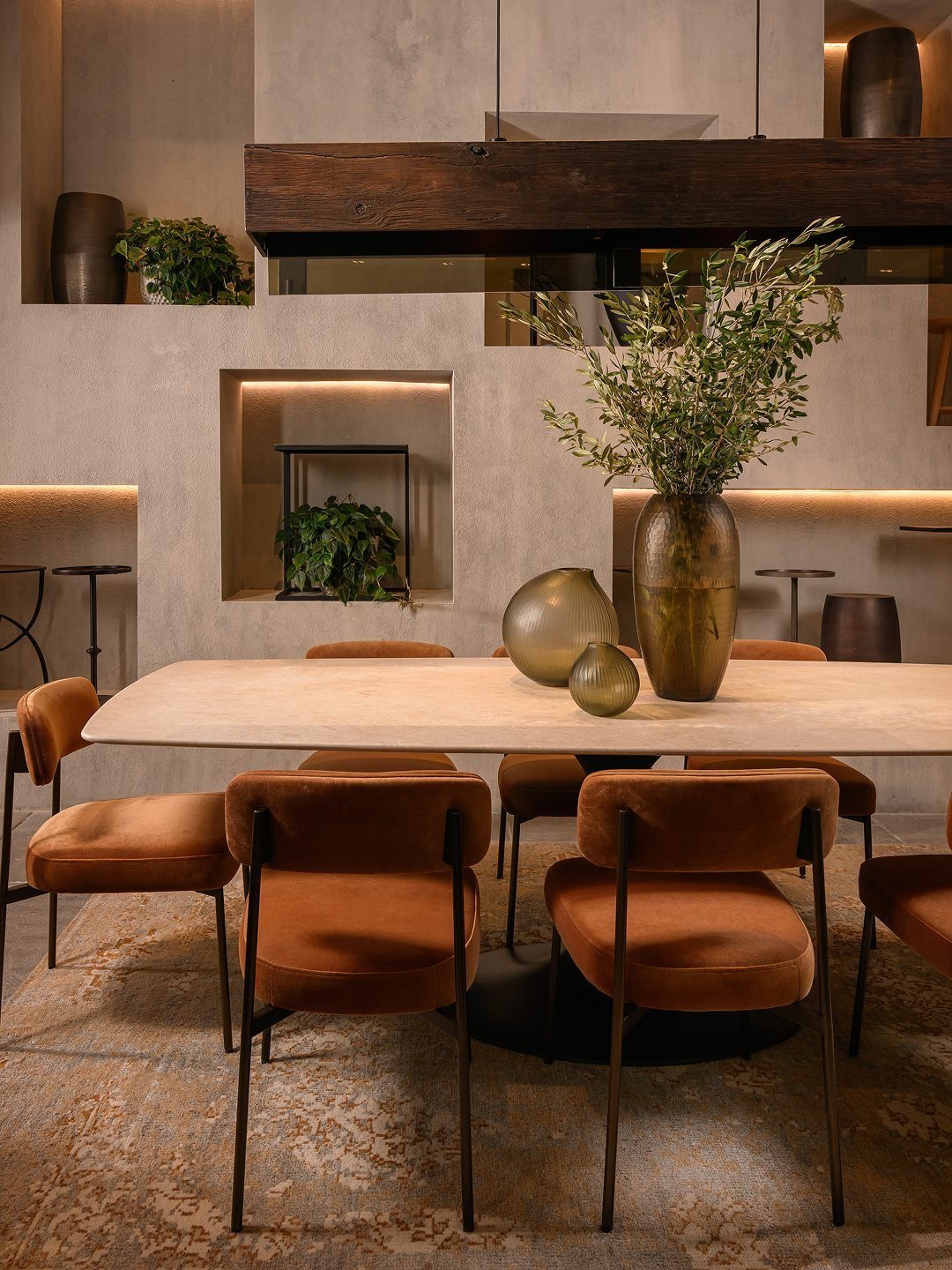 Orange velvet dining chairs surrounding a light stone table with greenery in a moody room.