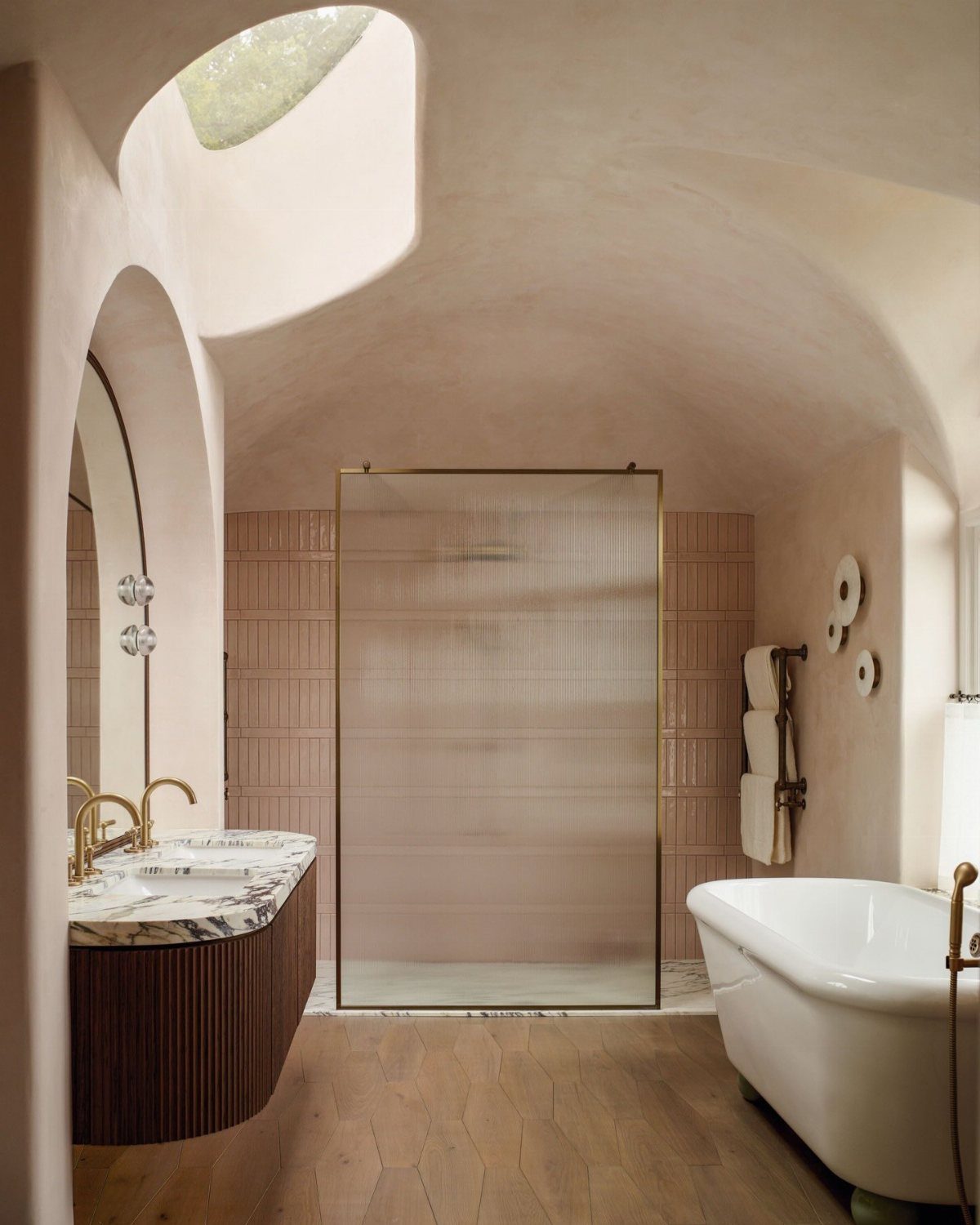 A curved plaster bathroom featuring a skylight, glass shower, marble vanity, and white bathtub.