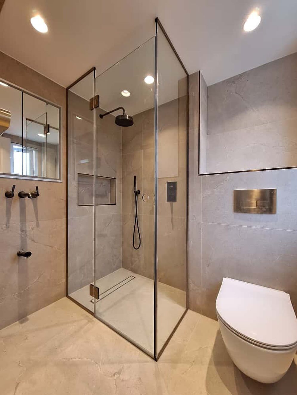 Clear glass shower enclosure with black metal trim and beige stone tiles in a modern bathroom.