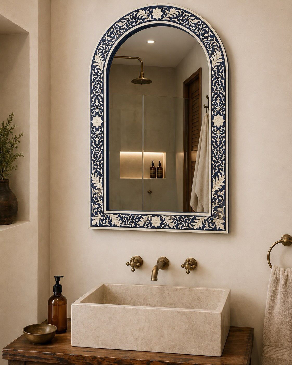 Arched mirror with blue patterned frame hanging above a stone sink and brass bathroom fixtures.