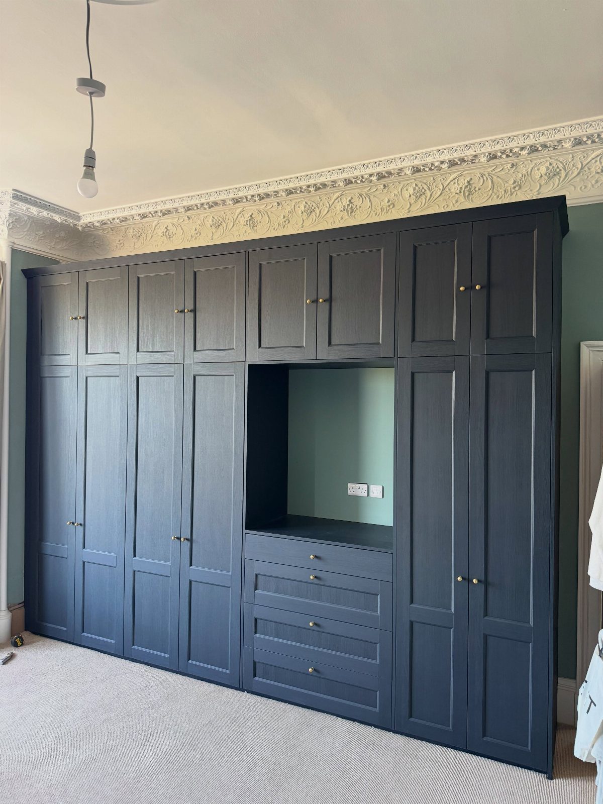 Navy blue built-in wardrobes with a central desk area and gold hardware in a bright room.