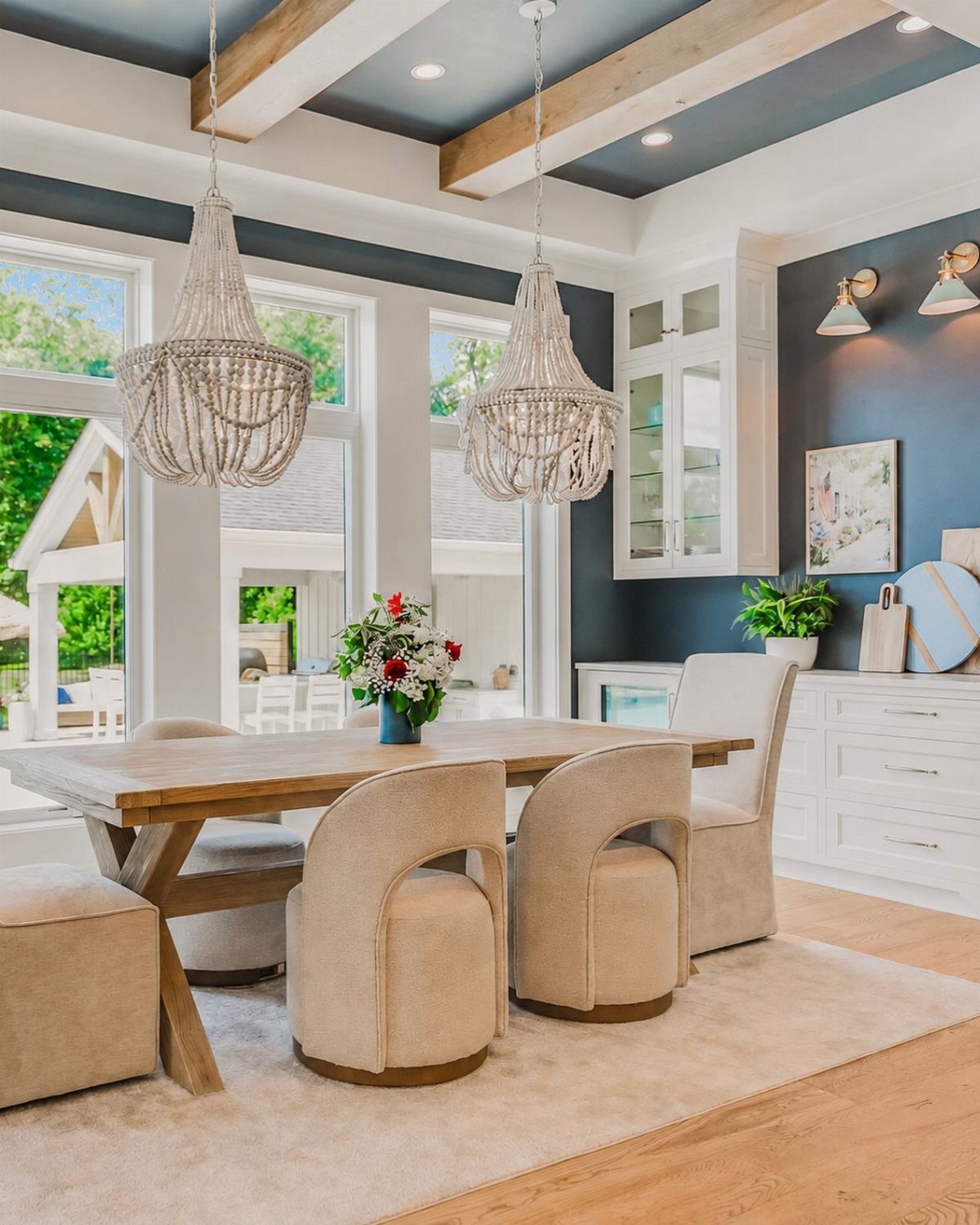 Navy blue ceiling with light wood beams and white beaded chandeliers over a dining table.