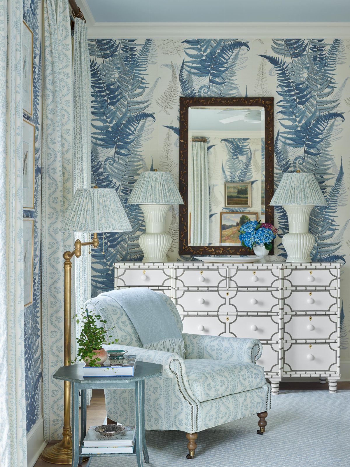Blue fern patterned wallpaper, a white patterned dresser, and a light blue armchair in a bright room.