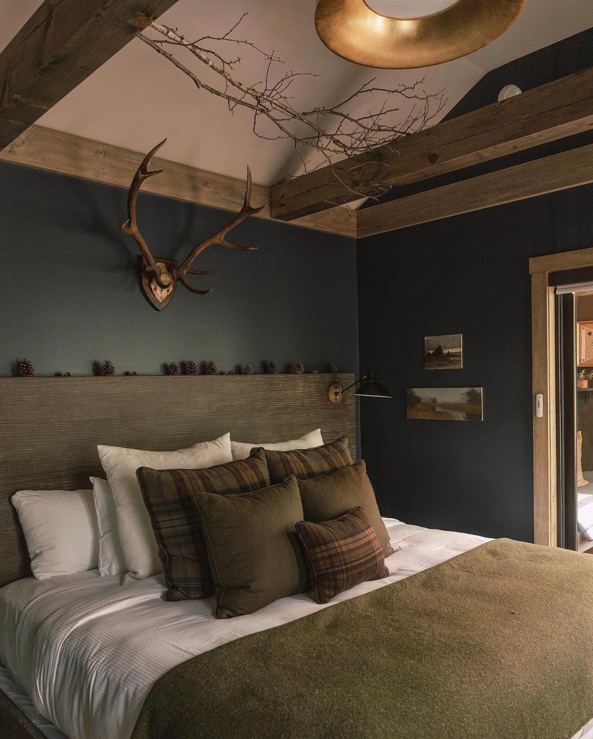 A bedroom with navy blue walls, wooden ceiling beams, and a bed with earth-toned pillows.