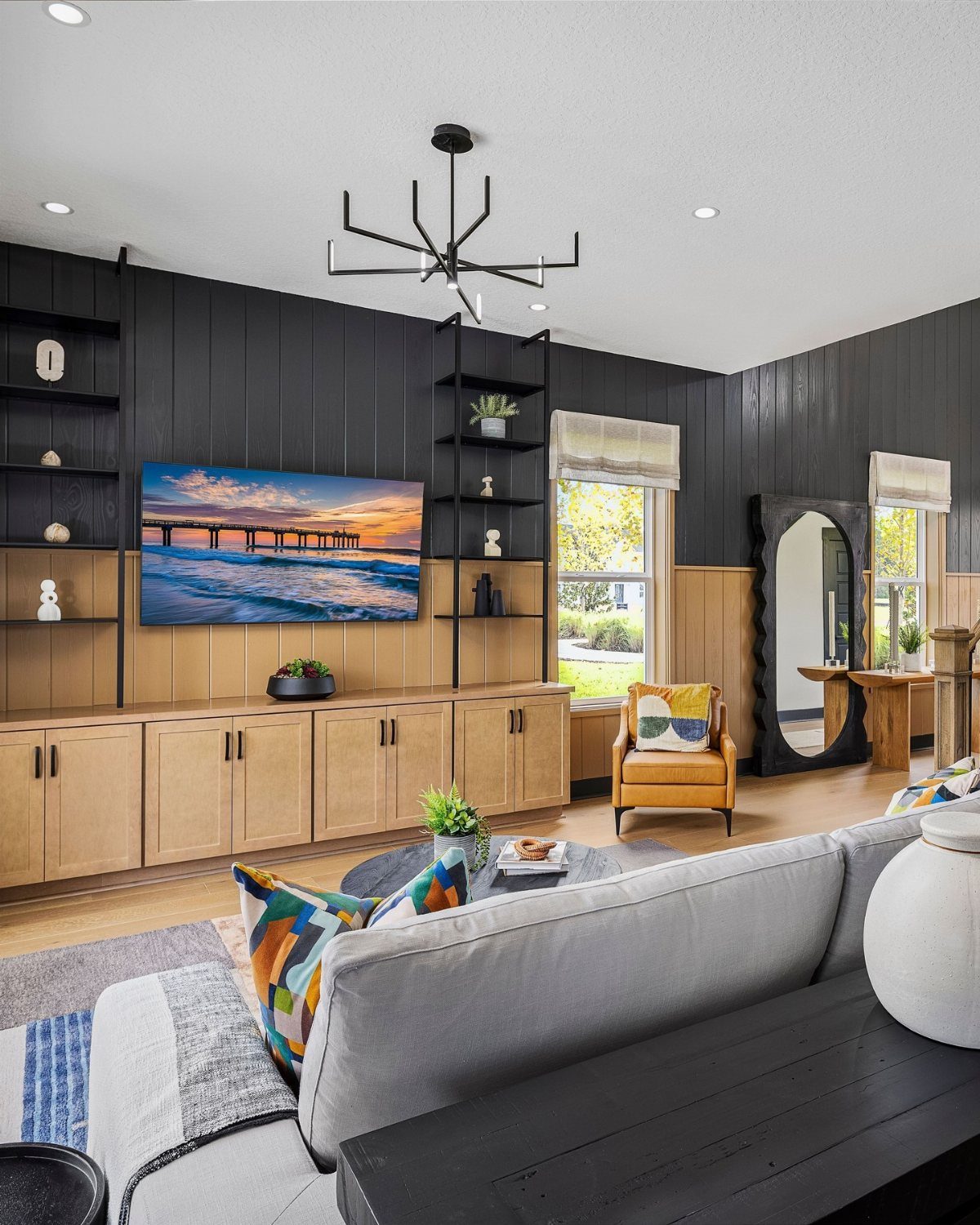 Modern living room with light wood cabinets, grey sofa, and black paneled walls.